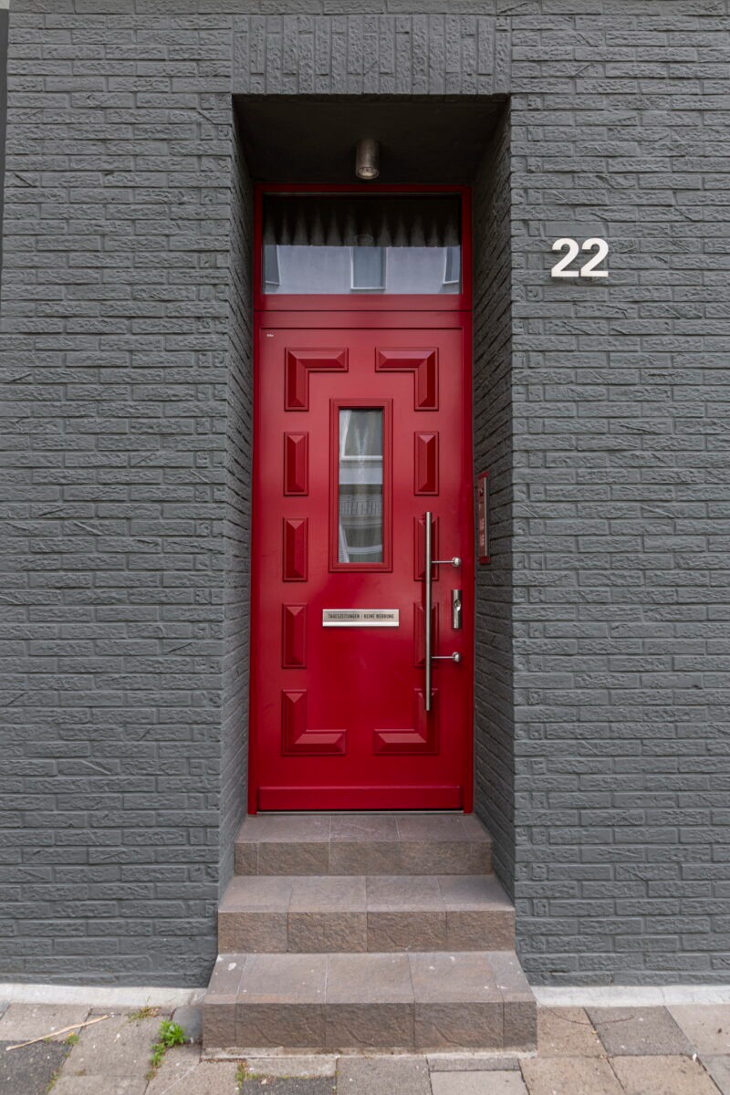 Rote Haustür als Kontrast in moderner grauer Fassade Rote Hauseingangstür mit geometrischen Verzierungen in grauer Klinkerfassade und der Hausnummer 22.
