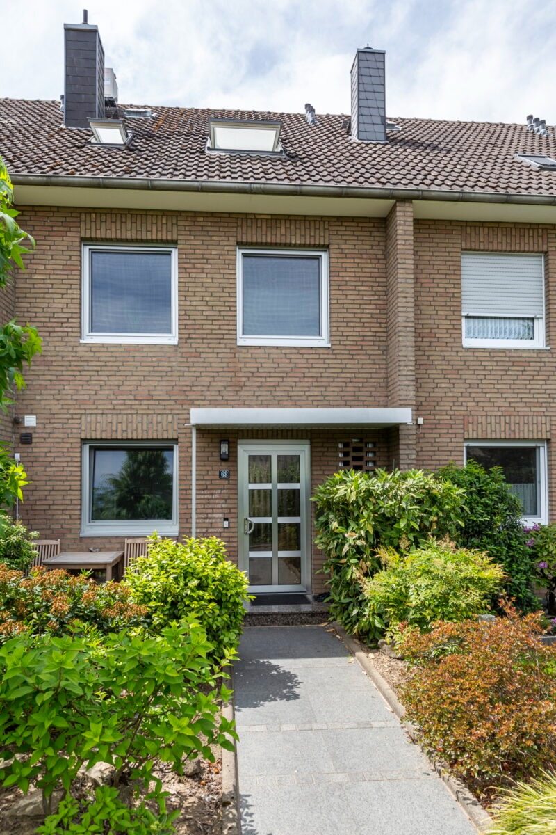 Reihenhaus mit gepflegtem Vorgarten und moderner Eingangstür Eingang eines Reihenhauses mit Klinkerfassade, Glas-Haustür, Vorgarten und Sitzbereich im Grünen.