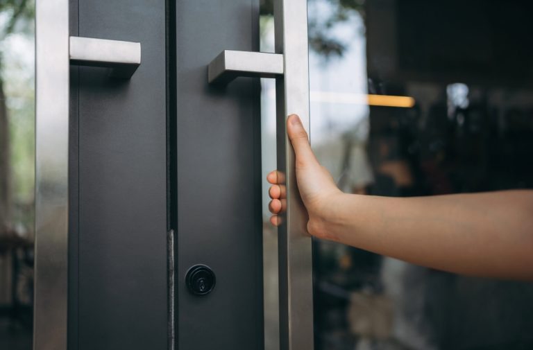 Moderne Eingangstür – Design trifft Funktionalität Nahaufnahme einer Hand, die eine moderne Tür mit Edelstahlgriff öffnet.