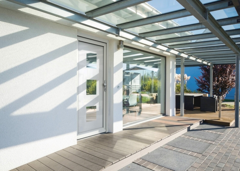 Weru 4 Moderne Haustür aus weißem Kunststoff mit Glaseinsätzen, Glasüberdachung und angrenzender Terrasse mit Holz- und Steinboden.