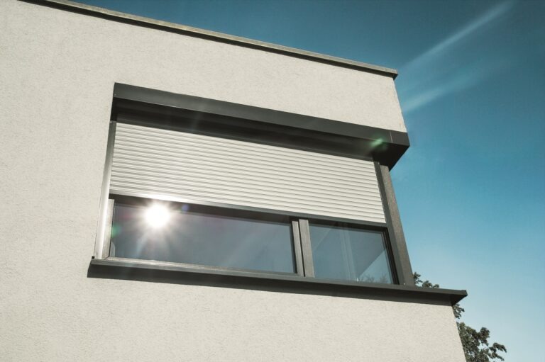 Moderne Rollladenlösung für optimalen Sonnen- und Sichtschutz Modernes Fenster eines Gebäudes mit halb geschlossenem Rollladen und Sonnenreflexion im Glas unter blauem Himmel.