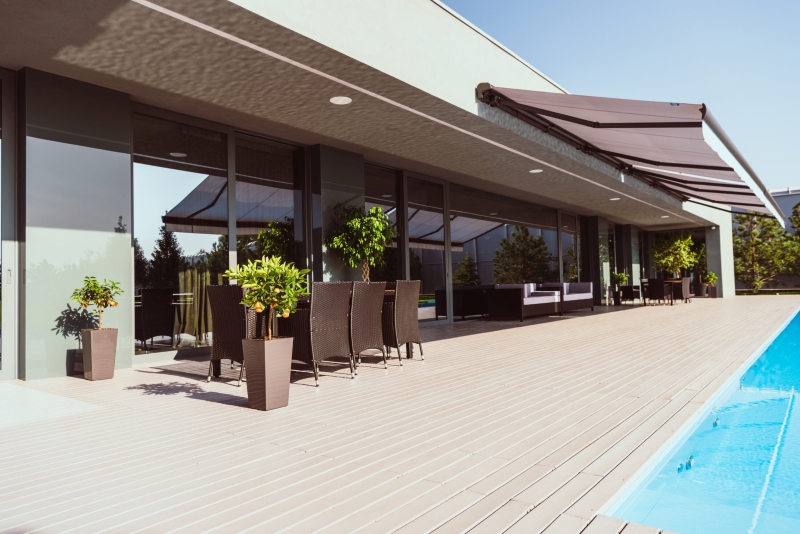 markilux 2 Moderne Terrasse mit Pool, dunklen Markisen, Sitzmöbeln und Pflanzen in Töpfen vor einer Glasfassade.