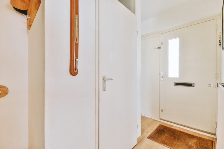 Freundlicher Eingangsbereich mit schlichter Weißgestaltung Heller Eingangsbereich einer Wohnung mit weißer Haustür, Garderobe und brauner Fußmatte auf Holzfußboden.