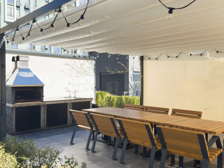 Gemütlicher Grillbereich mit moderner Pergola und Sitzgruppe Überdachte Terrasse mit großem Holztisch, Sitzbänken und gemauerter Grillstation unter einer modernen Pergola.