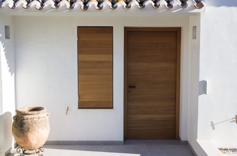 Mediterraner Hauseingang mit Holzdetails und heller Fassade Eingangsbereich eines mediterranen Hauses mit Holztür, passendem Fensterladen und heller Putzfassade.