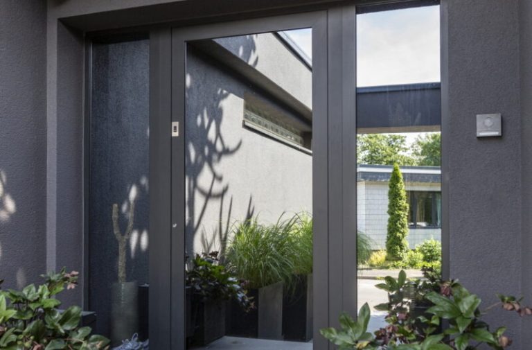 KOWA 5 Moderner Hauseingang mit grauer Glasfront-Tür, Pflanzenkübeln und klarer Architektur in Anthrazittönen.