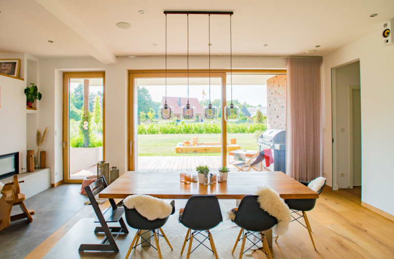 KOWA 3 Helles Esszimmer mit großen Holzfenstern und Schiebetüren, Blick auf Garten und Terrasse mit Grillplatz.